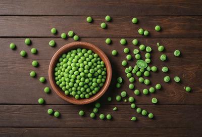 The primary subject of the image is a bowl filled with green peas. The bowl is placed on a wooden table, which serves as the setting. The visual style of the image is a photo, capturing the natural colors and textures of the peas. The dominant colors in the image are green, which is the color of the peas, and brown, which is the color of the wooden table. The overall atmosphere of the image is fresh and natural, as it showcases the simple beauty of the green peas.