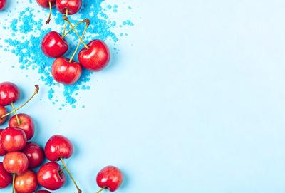 Cherries are the primary subject of the image, with a close-up view of the fruit. The setting is a blue background, which adds a vibrant and lively atmosphere to the scene. The visual style is a photo, capturing the details and colors of the cherries. The dominant colors are red and blue, creating a striking contrast between the cherries and the background.