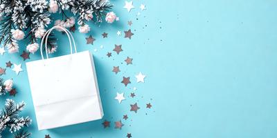 The primary subject of the image is a white shopping bag with stars on it. The bag is placed on a blue surface, which serves as the setting or background. The visual style of the image is a combination of photo and digital art, creating a unique and eye-catching design. The dominant colors in the image are white and blue, giving it a clean and fresh appearance.