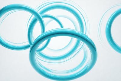 The primary subject of the image is a group of blue rings or circles. These rings are arranged in a circular pattern, with some overlapping each other. The setting is a white background, which provides a clean and minimalist appearance. The visual style is a combination of photo and digital art, as the rings appear to be digitally created and placed on the white surface. The dominant colors are blue, which gives the image a calm and soothing atmosphere.