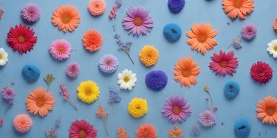 The primary subject of the image is a collection of colorful flowers, including pink, yellow, orange, and purple, arranged on a blue surface. The flowers are placed in various positions, creating a visually appealing and vibrant display. The setting appears to be a studio or a workspace, where the artist has carefully arranged the flowers to create a visually striking composition. The overall atmosphere of the image is lively and cheerful, with the bright colors and diverse flower types contributing to the dynamic and engaging visual