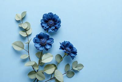 The primary subject of the image is a bouquet of three blue flowers, each with a green leaf, arranged together. The flowers are placed on a blue background, which adds a sense of depth and contrast to the scene. The visual style of the image is a close-up of the flowers, showcasing their details and colors. The dominant colors in the image are blue and green, creating a calm and serene atmosphere.