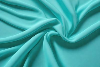 The primary subject of the image is a close-up of a piece of blue fabric. The setting is a blue background, which creates a visually appealing contrast with the fabric. The visual style is a photo, capturing the intricate details of the fabric. The colors and mood of the image are predominantly blue, creating a calm and serene atmosphere.