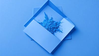 The primary subject of the image is a blue box filled with blue powder. The setting is a blue background, which creates a visually appealing contrast with the blue box. The visual style is a close-up of the box, showcasing the powder inside. The colors and mood of the image are predominantly blue, giving it a calm and serene atmosphere.