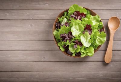 The primary subject of the image is a bowl filled with fresh green lettuce. The bowl is placed on a wooden table, which serves as the setting for the scene. The visual style of the image is a photo, capturing the vibrant colors and details of the lettuce. The dominant colors in the image are green, which is the color of the lettuce, and brown, which is the color of the wooden table. The overall atmosphere of the image is fresh and healthy, as it showcases a nutritious