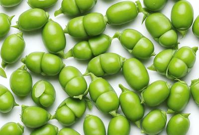 The primary subject of the image is a large group of green peas. They are arranged in a pattern on a white surface, creating a visually appealing and colorful display. The setting appears to be a studio or a controlled environment, as the peas are neatly arranged and the background is white. The visual style of the image is a close-up of the peas, showcasing their vibrant green color and unique shape. The overall atmosphere of the image is fresh, lively, and inviting.
