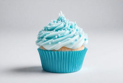 The primary subject of the image is a cupcake with blue frosting and white sprinkles. The cupcake is placed on a white surface, which serves as the background. The visual style of the image is a photo, capturing the details of the cupcake and its decorations. The dominant colors in the image are blue and white, creating a visually appealing and festive atmosphere.
