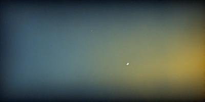 The primary subject of the image is a moon, which is the main object in the scene. The setting is a dark, cloudy sky, with the moon being the only bright spot in the background. The visual style of the image is a photo, capturing the moon in its natural environment. The colors and mood of the image are predominantly dark and moody, with the moon being the only source of light in the scene.