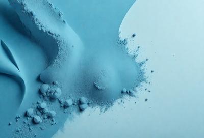 The primary subject of the image is a blue substance, possibly a powder or a liquid, that is spreading or dripping onto a white surface. The setting appears to be a studio or a controlled environment, as the blue substance is being carefully applied. The visual style of the image is a combination of photo and digital art, as it captures the movement and texture of the blue substance. The colors and mood of the image are predominantly blue and white, creating a sense of calmness and precision.