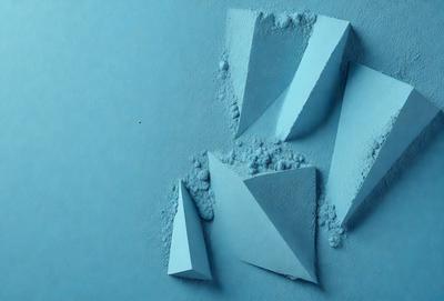 The primary subject of the image is a blue surface with three white, three-dimensional shapes or sculptures on it. The sculptures are made of a powdery substance, giving them a unique appearance. The setting appears to be a blue background, which complements the sculptures and adds to the overall visual style. The colors and mood of the image are predominantly blue, creating a calm and serene atmosphere.