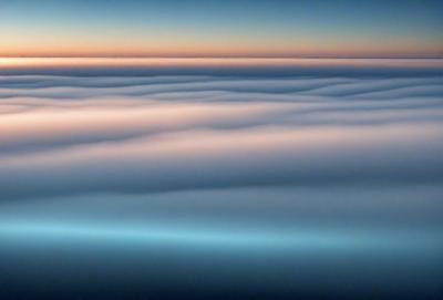 The primary subject of the image is a cloudy sky, with a blue hue. The setting is a vast expanse of the sky, with no visible land or other objects. The visual style is a natural, outdoor scene, and the colors and mood convey a sense of tranquility and vastness.
