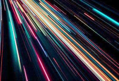 The primary subject of the image is a brightly colored, colorful light streak or blur. The setting is a dark background, which contrasts with the vibrant colors of the light streak. The visual style appears to be a digital art or illustration, as the colors and light streak are not realistic in a photo. The dominant colors are bright and vivid, creating a lively and energetic atmosphere.