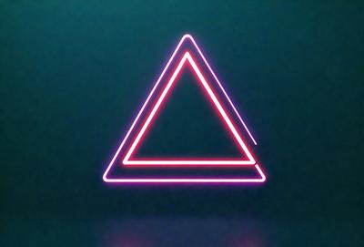 The primary subject of the image is a neon pink triangle. The setting is a dark background, which contrasts with the bright pink triangle. The visual style is digital art, as the triangle is created using a computer program. The colors and mood of the image are vibrant and energetic, with the pink triangle standing out against the dark background.
