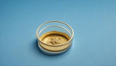 The primary subject of the image is a small glass bowl filled with a yellow substance, likely a powder or a granular material. The bowl is placed on a blue surface, which serves as the setting or background. The visual style of the image is a close-up, focusing on the details of the bowl and its contents. The colors in the image are predominantly yellow and blue, creating a warm and inviting atmosphere.