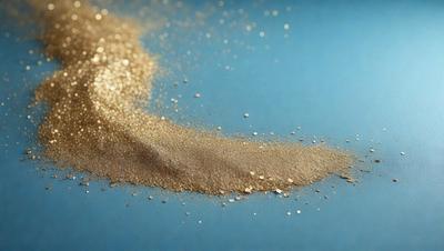 The primary subject of the image is a pile of gold glitter, which is the main focus of the scene. The setting is a blue surface, which serves as the backdrop for the glitter. The visual style of the image is a close-up of the glitter, showcasing its texture and shine. The colors in the image are predominantly gold, giving the scene a warm and shiny atmosphere.