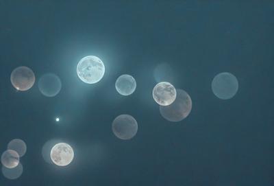 The primary subject of the image is a group of moons, which are floating in the dark sky. The setting is a nighttime scene with a clear, cloudless sky. The visual style is a combination of a photo and digital art, creating a unique and captivating representation of the moons. The colors and mood of the image are predominantly dark and moody, with the moons being the main source of light in the scene.