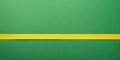 The primary subject of the image is a yellow strip of paper or tape, which is placed on a green background. The setting appears to be a table or a surface where the paper is placed. The visual style of the image is a close-up of the yellow strip, emphasizing its color and texture. The colors and mood of the image are predominantly green and yellow, creating a warm and vibrant atmosphere.