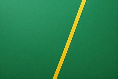 The primary subject of the image is a yellow line on a green background. The setting is a large, open space with a green surface. The visual style is a combination of digital art and illustration, creating a unique and eye-catching design. The colors and mood of the image are predominantly green and yellow, giving it a vibrant and lively appearance.
