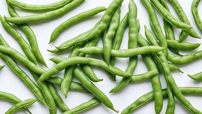 The primary subject of the image is a close-up of green beans, which are the main objects in the scene. The beans are arranged on a white surface, creating a clean and simple visual style. The colors in the image are predominantly green, which gives the scene a fresh and natural atmosphere.