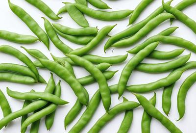 The primary subject of the image is a large group of green beans, which are the main objects in the scene. The beans are arranged in a pattern on a white background, creating a visually appealing and colorful display. The visual style of the image is a close-up of the beans, showcasing their texture and details. The colors and mood of the image are predominantly green, with the beans being the main focus and creating a fresh and vibrant atmosphere.