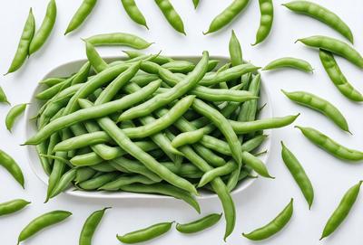 The primary subject of the image is a white plate filled with green beans. The plate is placed on a white surface, which creates a clean and simple visual style. The green beans are the main focus of the image, and they are arranged in a way that fills the entire plate. The colors and mood of the image are predominantly green, which gives it a fresh and natural atmosphere.