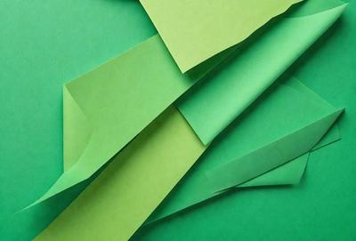 The primary subject of the image is a green paper, which is the main object, scene, or focus of the image. The setting is a green background, which complements the green paper. The visual style is a close-up of the green paper, showcasing its texture and color. The colors and mood of the image are predominantly green, creating a calm and serene atmosphere.
