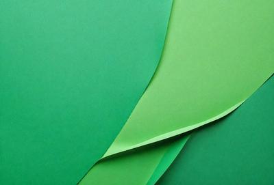 The primary subject of the image is a green paper, which is the main object, scene, or focus of the image. The setting/background consists of a green surface, which is visible in the image. The visual style is a photo, as the image is a close-up of the green paper. The colors and mood of the image are predominantly green, giving it a calm and serene atmosphere.