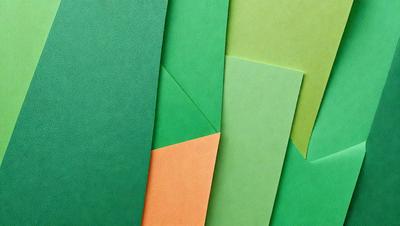 The primary subject of the image is a collection of green and orange colored paper. The setting is a table, and the visual style is a close-up of the paper. The colors and mood of the image are vibrant and lively, with the green and orange colors creating a sense of freshness and energy.