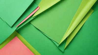 The primary subject of the image is a stack of green paper. The setting is a table, and the visual style is a close-up of the green paper. The colors and mood of the image are predominantly green, creating a calm and natural atmosphere.