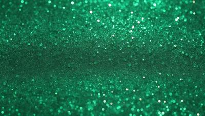The primary subject of the image is a close-up of a green glittery surface, possibly a wall or a piece of fabric. The setting appears to be indoors, with the green glittery surface being the main focus of the image. The visual style is a close-up, which emphasizes the glittery texture of the surface. The colors and mood of the image are predominantly green, with the glittery surface adding a sense of sparkle and shine to the overall atmosphere.