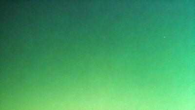 The primary subject of the image is a large, bright green background. The setting is a dark, empty space, with no visible objects or people. The visual style appears to be a photo, as it captures the vibrant color of the green background. The colors and mood of the image are lively and energetic, with the green hue creating a sense of freshness and vitality.