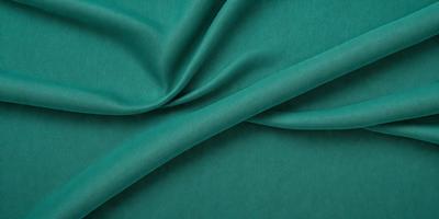 The primary subject of the image is a piece of green fabric, which is the main object, scene, or focus of the image. The setting or background of the image is a dark blue surface, which contrasts with the green fabric. The visual style of the image is a close-up of the green fabric, showcasing its texture and details. The colors and mood of the image are predominantly dark blue and green, creating a calm and serene atmosphere.