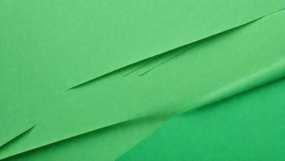 The primary subject of the image is a green piece of paper. The setting is a table, and the visual style is a close-up of the green paper. The colors and mood of the image are predominantly green, creating a calm and serene atmosphere.