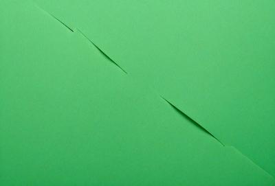 The primary subject of the image is a green sheet of paper with a cut in it. The cut is located in the middle of the paper, creating a triangular shape. The setting is a table, and the visual style appears to be a photo. The colors in the image are predominantly green, giving the scene a calm and natural atmosphere.