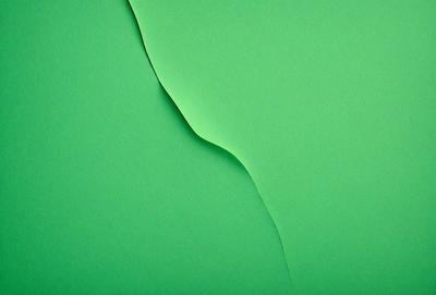 The primary subject of the image is a green sheet of paper with a cutout in the shape of a triangle. The cutout is located in the middle of the sheet, and the paper appears to be a part of a larger green surface. The visual style of the image is a close-up of the green paper with the cutout, showcasing the details of the triangle shape. The colors and mood of the image are predominantly green, giving it a calm and natural atmosphere.
