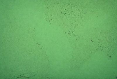 The primary subject of the image is a green surface, which appears to be a piece of green fabric or a green wall. The setting is indoors, with the green surface being the main focus of the image. The visual style is a close-up of the green surface, showcasing its texture and color. The colors and mood of the image are predominantly green, creating a calm and soothing atmosphere.