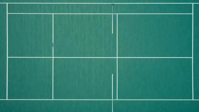 The primary subject of the image is a tennis court, which is a large, rectangular surface with white lines. The setting is an outdoor environment, and the visual style is a photo. The court is surrounded by a blue surface, which adds to the overall atmosphere of the image.