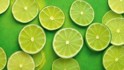 The primary subject of the image is a group of green limes. They are arranged on a green surface, which could be a table or a counter. The limes are sliced and placed in various positions, creating a visually appealing display. The overall atmosphere of the image is fresh and vibrant, with the green limes being the main focus.