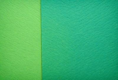The primary subject of the image is a green and a lime green fabric. The setting is a wall, and the visual style is a close-up of the fabric. The colors and mood of the image are vibrant and lively, with the green fabrics being the main focus.