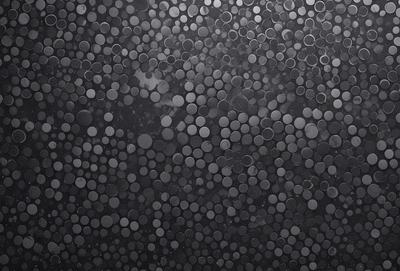 The primary subject of the image is a pattern of circles, which are arranged in a visually appealing manner. The setting is a black background, which contrasts with the circles, making them stand out. The visual style of the image is a combination of photo and digital art, as it appears to be a close-up of a pattern, possibly a texture or a texture-like pattern. The dominant colors in the image are black and white, with the circles being the main focus and the background providing a stark contrast. The overall atmosphere of