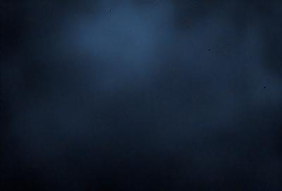 The primary subject of the image is a dark, cloudy sky. The setting is a nighttime scene with a black background. The visual style is a photo, capturing the beauty of the night sky. The colors and mood are predominantly dark and moody, with the clouds and sky creating a dramatic atmosphere.