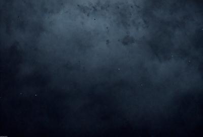 The primary subject of the image is the night sky, which is filled with stars. The setting is a dark, cloudy night, creating a dramatic and moody atmosphere. The visual style is a photo, capturing the beauty of the night sky and the stars. The colors and mood are predominantly dark and mysterious, with the stars providing a touch of brightness and wonder.