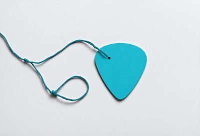 The primary subject of the image is a blue guitar pick hanging from a string. The setting is a white background, which provides a clean and uncluttered appearance. The visual style is a close-up of the guitar pick, emphasizing its color and texture. The dominant colors are blue and white, creating a calm and soothing atmosphere.