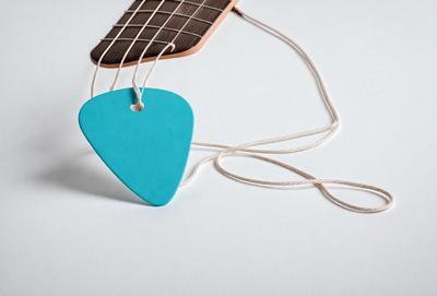 The primary subject of the image is a blue guitar pick hanging from a string. The setting is a white background, and the visual style appears to be a photo. The dominant colors are blue and white, creating a calm and soothing atmosphere.