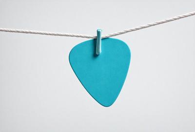 The primary subject of the image is a blue guitar pick hanging from a string. The setting is a white background, and the visual style is a photo. The dominant colors are blue and white, creating a calm and soothing atmosphere.
