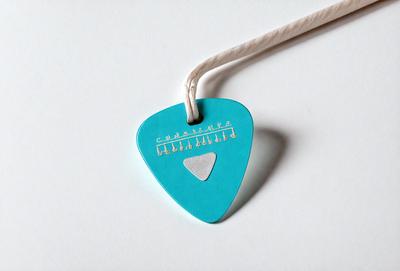 The primary subject of the image is a guitar pick with a blue background. The guitar pick is attached to a blue string, and it is hanging from a rope. The setting is a white background, which provides a clean and simple backdrop for the guitar pick. The visual style is a close-up of the guitar pick, showcasing its details and texture. The colors and mood of the image are predominantly blue, giving it a calm and soothing atmosphere.