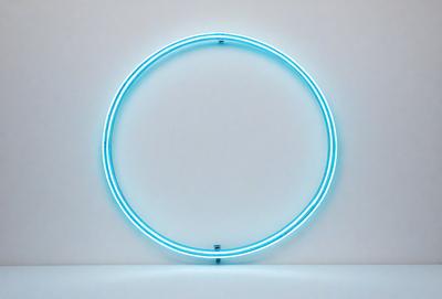 The primary subject of the image is a large, illuminated circle, which appears to be a light fixture or a neon sign. The circle is blue and is mounted on a white wall. The setting is a plain white wall, which serves as the background for the circle. The visual style of the image is a close-up of the circle, emphasizing its shape and color. The colors and mood of the image are predominantly blue and white, creating a clean and modern atmosphere.