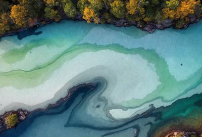 The primary subject of the image is a body of water, possibly a lake or a river, with a blue-green color. The setting is a natural environment, with trees and rocks visible in the background. The visual style appears to be a combination of a photo and a drawing, creating a unique and artistic representation of the water. The colors and mood of the image are serene and calming, with the blue-green water and the surrounding natural elements creating a peaceful atmosphere.