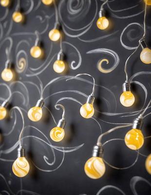 The primary subject of the image is a collection of yellow light bulbs hanging from strings. The setting is a black wall, which serves as the background for the hanging lights. The visual style of the image is a combination of digital art and illustration, as the yellow light bulbs are depicted in a creative and artistic manner. The dominant colors in the image are yellow, which gives the scene a warm and inviting atmosphere.