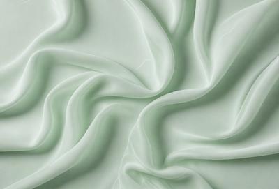 The primary subject of the image is a close-up of a green fabric, possibly a piece of clothing or a curtain. The setting is a white wall, which serves as the background for the fabric. The visual style appears to be a photo, as the fabric is captured in detail. The colors and mood of the image are predominantly green, giving it a calm and soothing atmosphere.